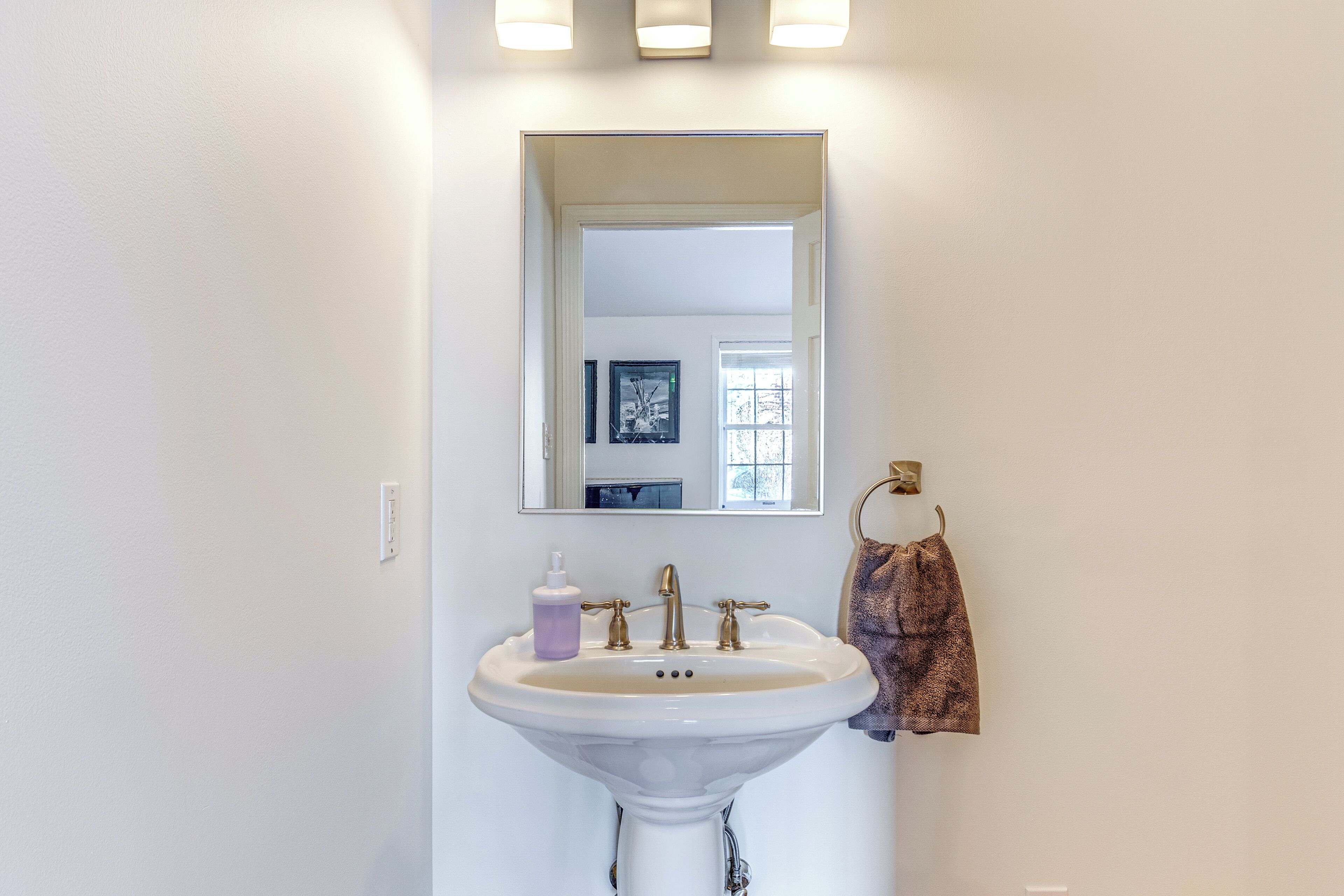 A bathroom with a white sink, a mirror, and a towel hanging on the wall.