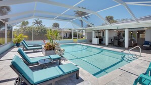 A covered outdoor pool area with lounge chairs, a small table, and a potted plant.