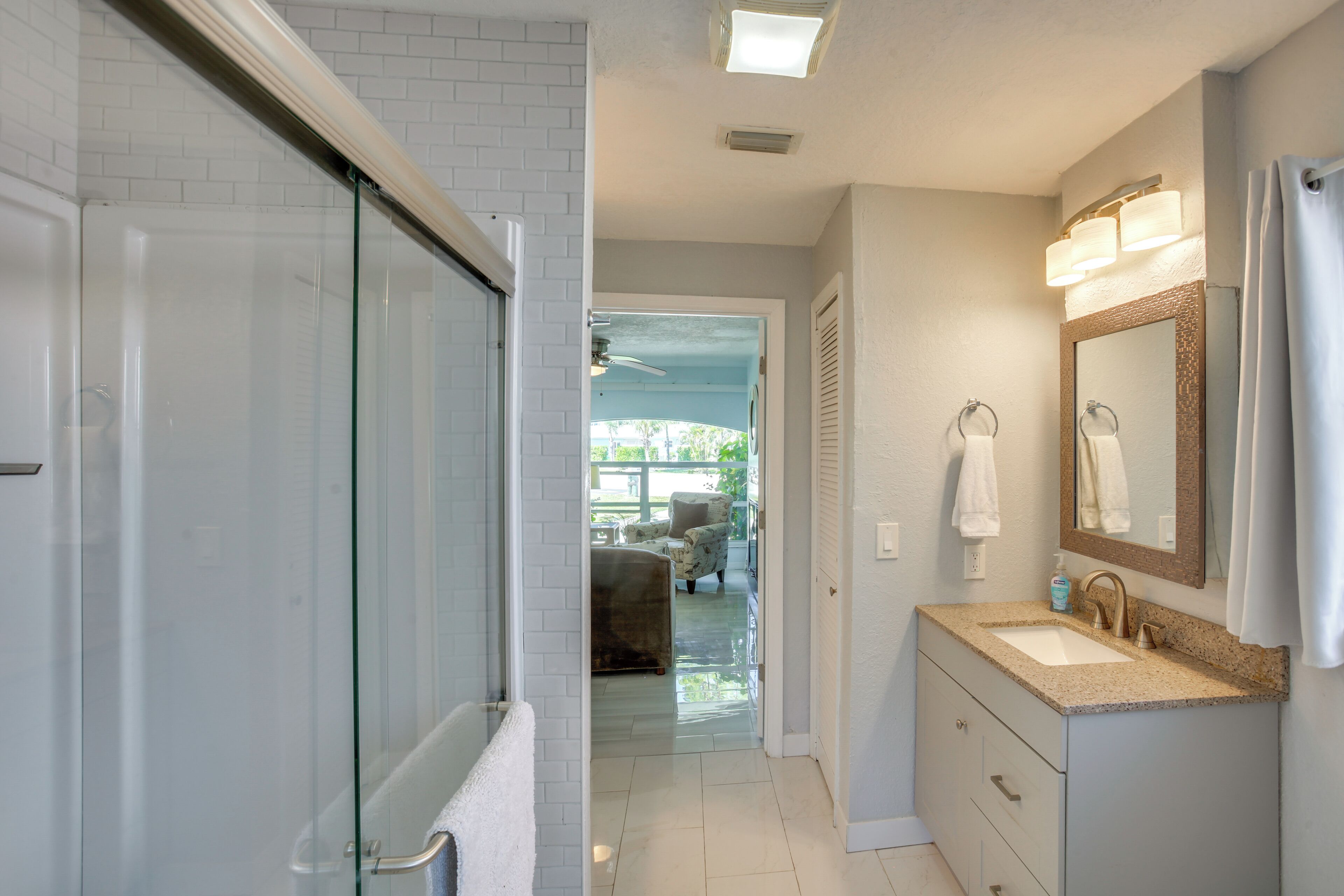 A bathroom with a glass shower enclosure, a sink with a vanity, and a mirror.
