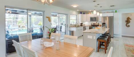 A modern kitchen with white cabinets, stainless steel appliances, and a wooden dining table.