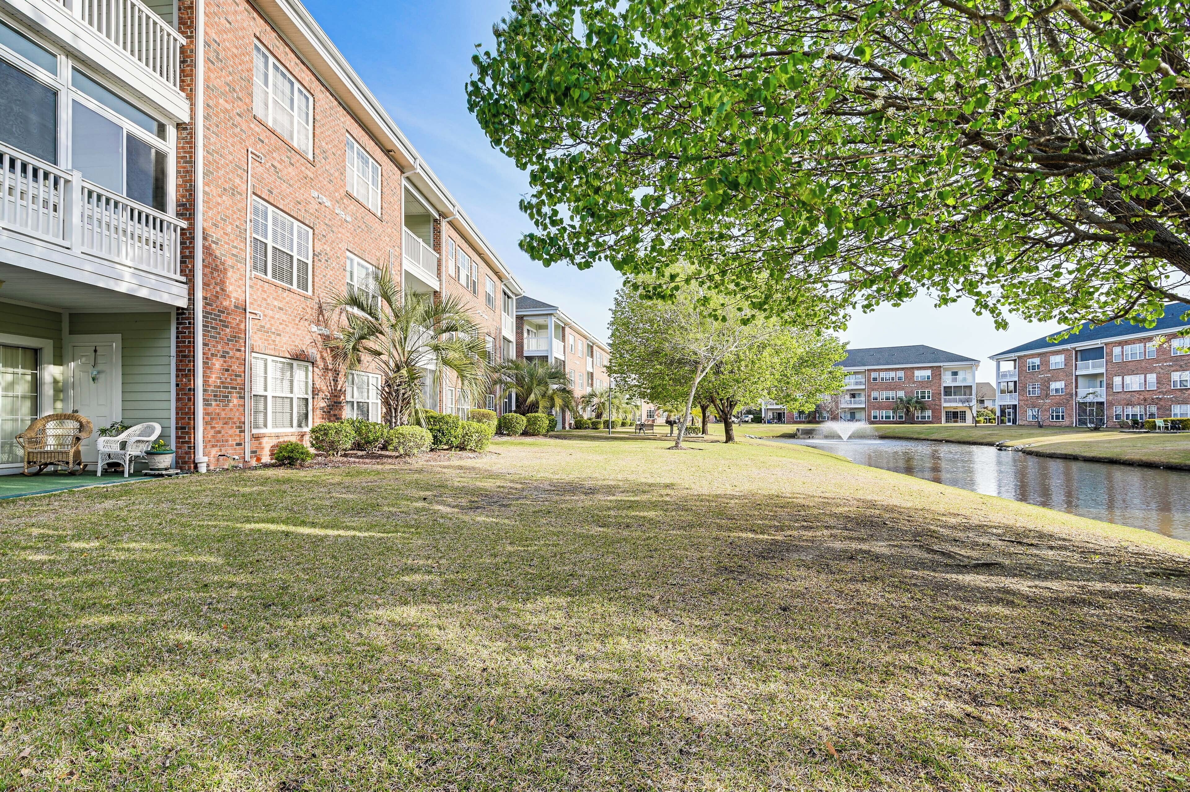 A residential building with a brick facade, a grassy lawn, and a small pond.