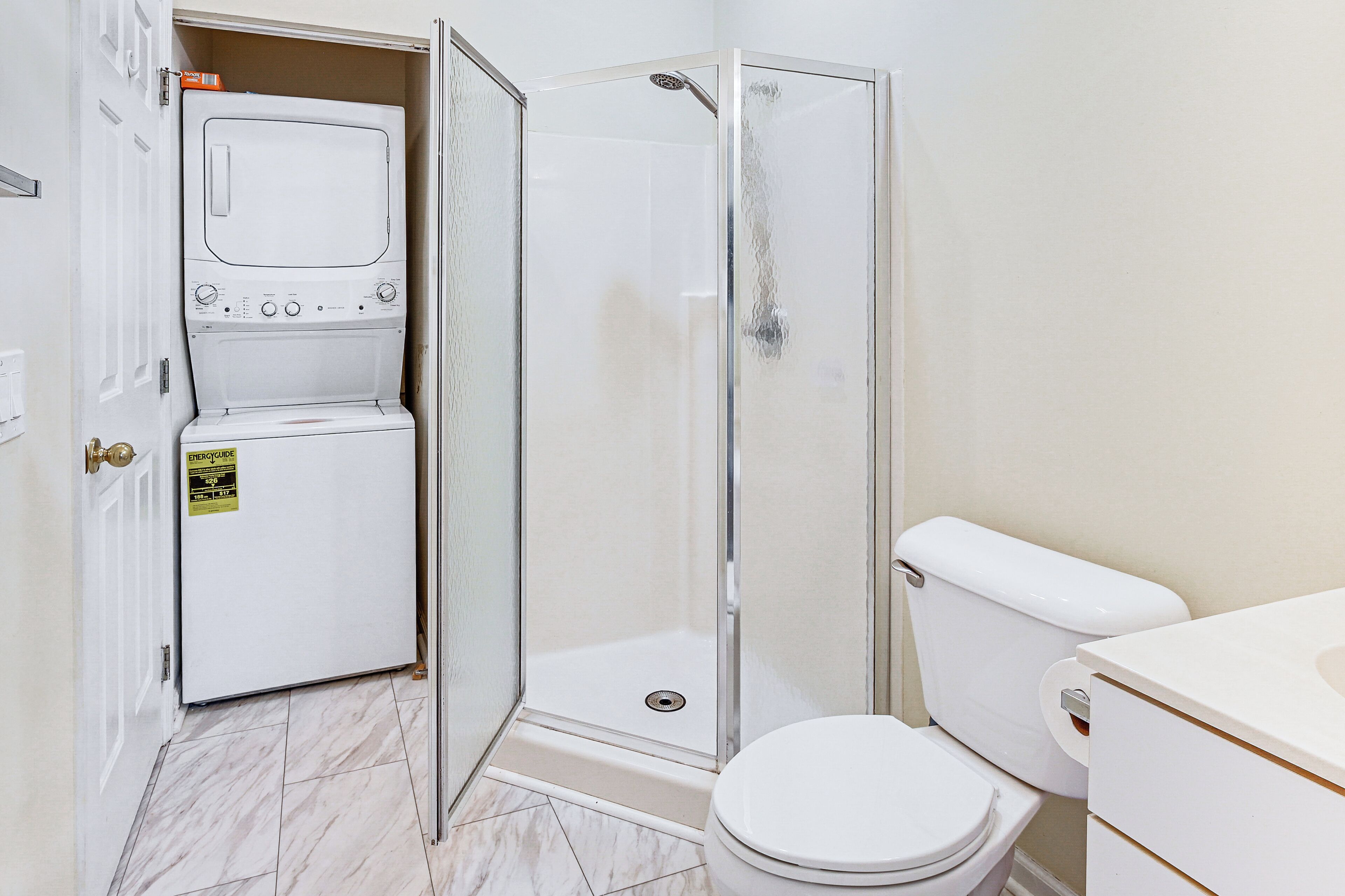 A compact bathroom with a shower, toilet, and a washing machine.