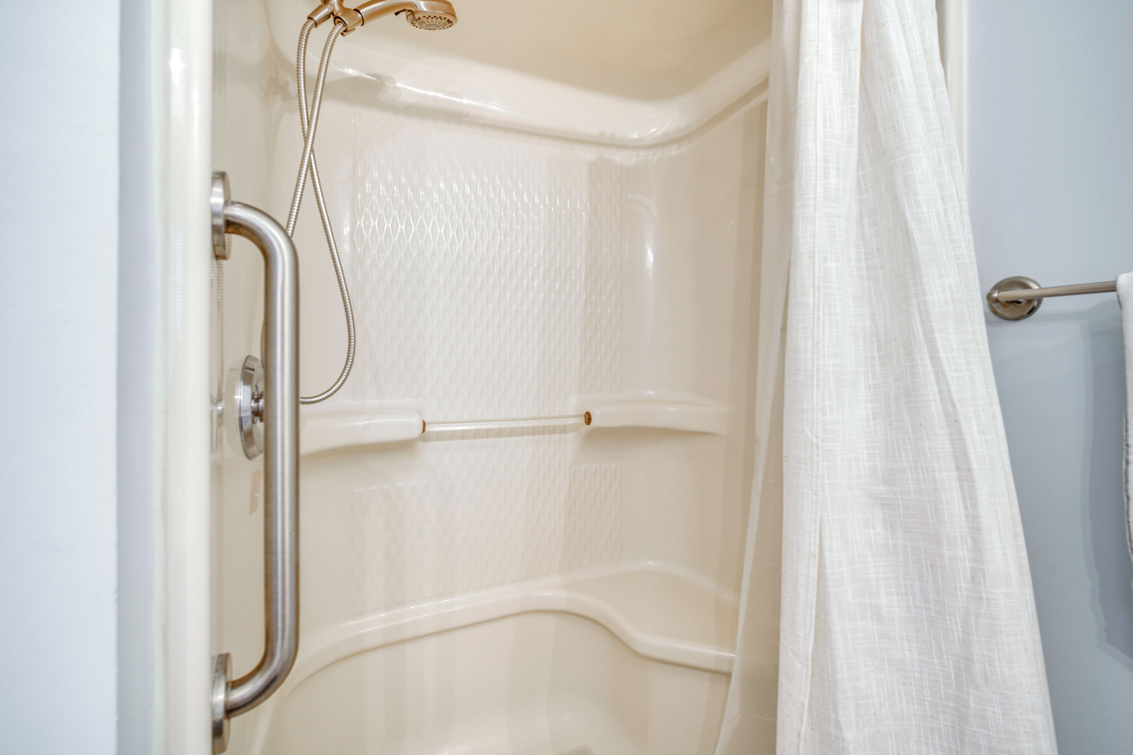 A shower area with a grab bar, a showerhead, and a curtain.