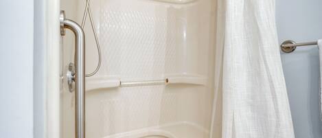 A shower area with a grab bar, a showerhead, and a curtain.