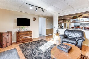 Uma sala de estar com televisão de tela plana, sofá de couro, mesa de centro de madeira e tapete estampado.