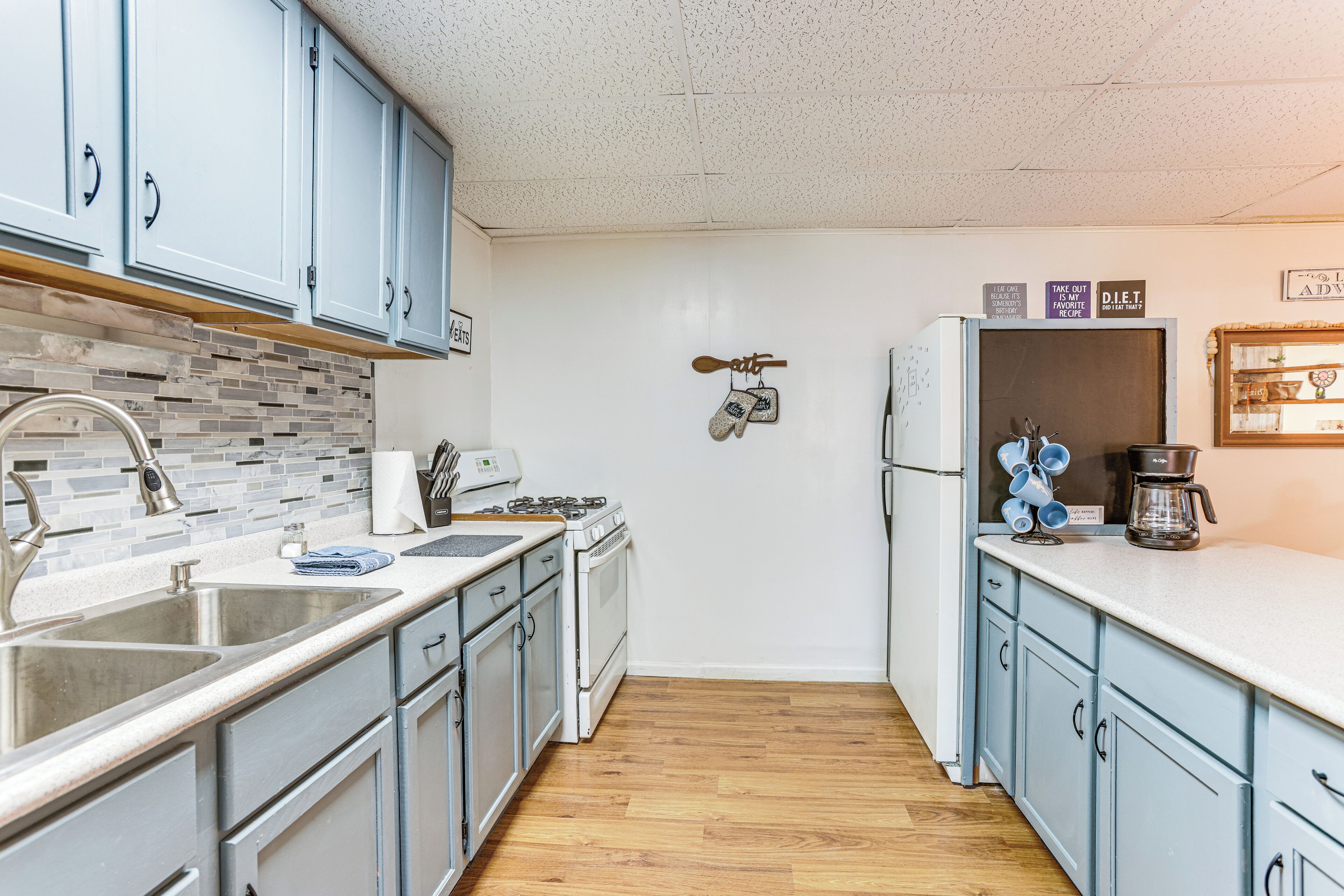 A kitchen with light blue cabinets, a white countertop, a wooden backsplash, a stove, and a refrigerator.