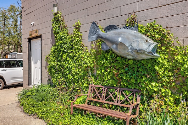 A building with a large fish sculpture, a bench, and a car parked nearby.