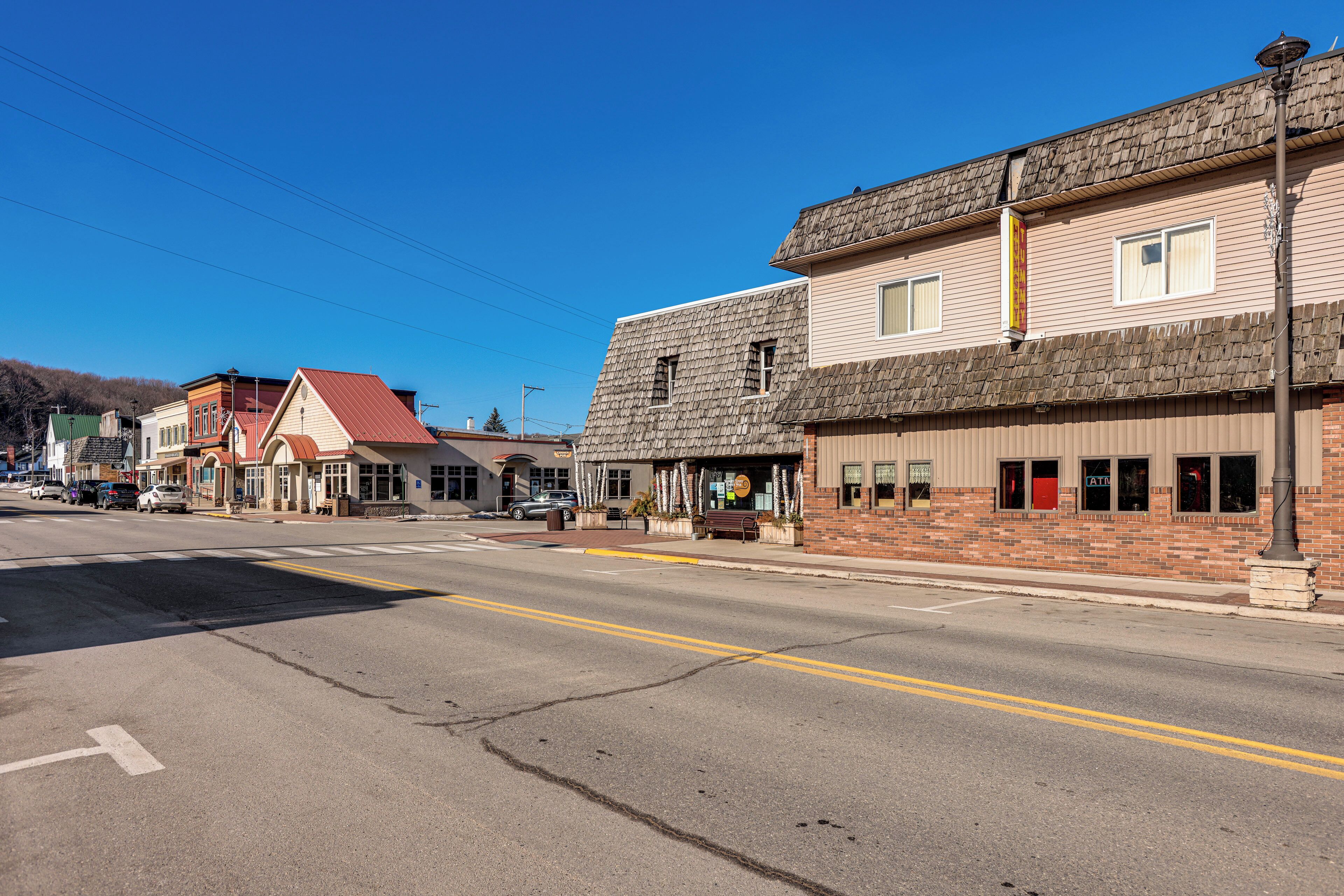 A street view with buildings, including a two-story brick building with a red door and a corner store with a sign.