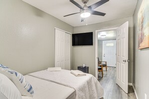A bedroom with two beds, a ceiling fan, a mounted TV, and a door leading to another room.