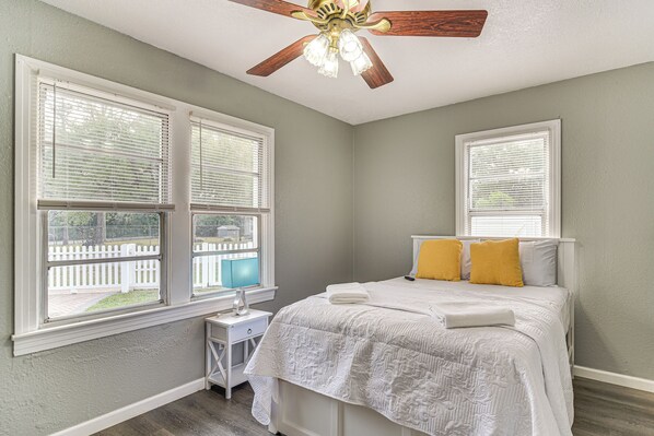 A bedroom with a bed, two windows, a nightstand, and a ceiling fan. - Breezy Tampa Home w/ Yard: Perfect for Long Stays (Lutz)