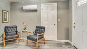 A room with two black leather chairs, a small table with flowers, a white door, and an air conditioning unit on the wall. - Breezy Tampa Home w/ Yard: Perfect for Long Stays (Lutz)