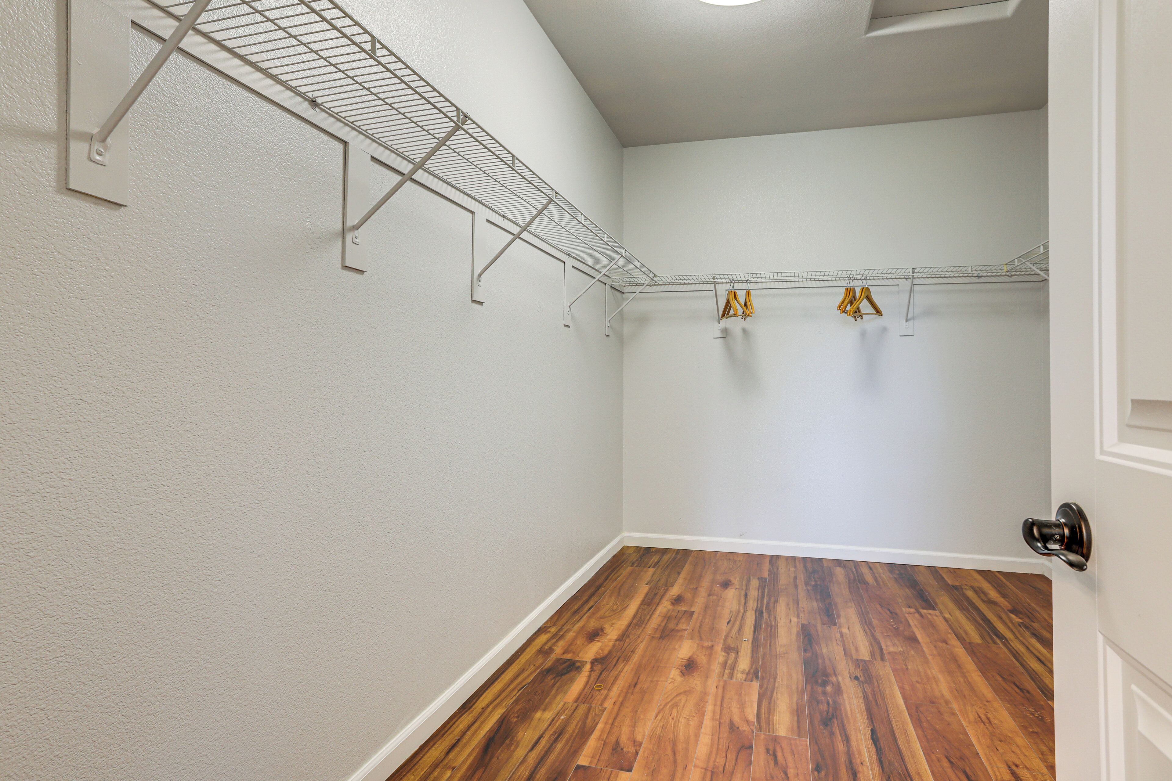 A room with a wooden floor, white walls, and a metal shelf with clothes hanging.