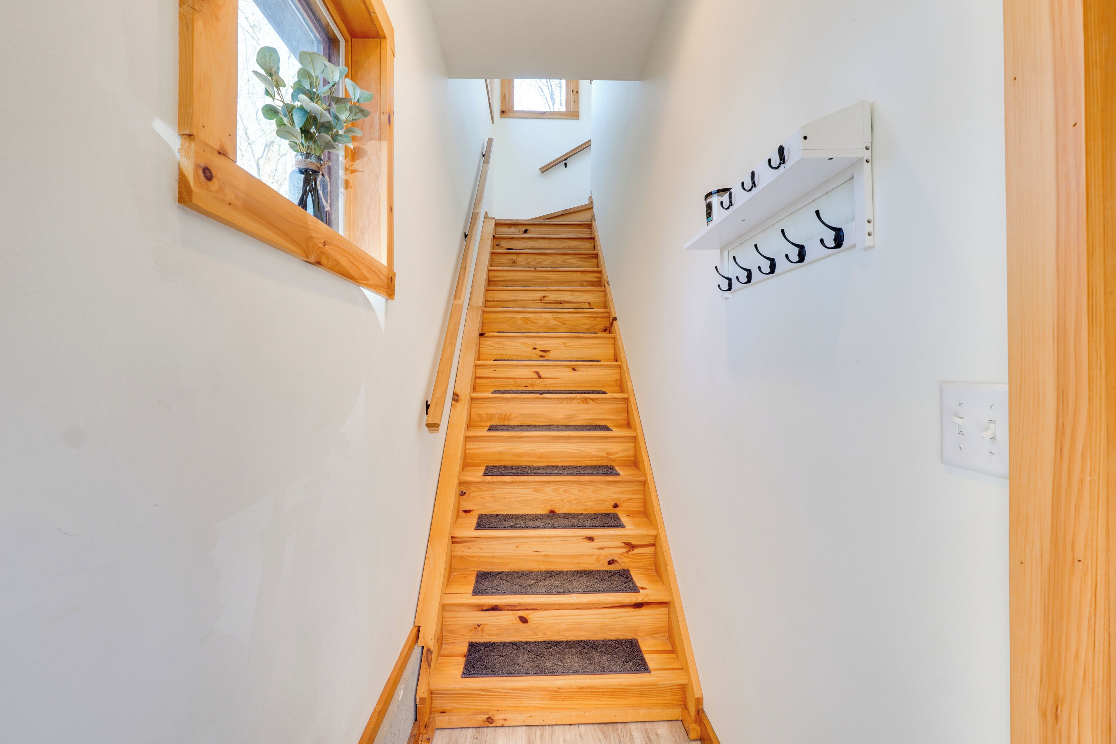 A wooden staircase with a handrail, a small window with a plant, and a wall-mounted hookboard.