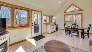 Une cuisine spacieuse avec des meubles en bois, une table à manger avec des chaises et de grandes fenêtres offrant une vue sur les arbres.