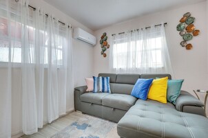 A living room with a grey sofa, white curtains, and a decorative plate wall art.
