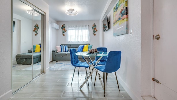 A modern living room with a glass dining table, blue chairs, and a grey sofa. - 2 Mi to Hard Rock Stadium: Studio in Miami Gardens (Miami Gardens)