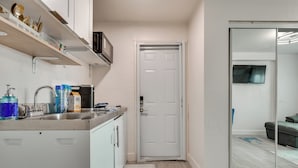 A compact kitchen with white cabinets, a stainless steel sink, and a microwave. A sliding glass door leads to a living area with a sofa and a coffee table. - 2 Mi to Hard Rock Stadium: Studio in Miami Gardens (Miami Gardens)