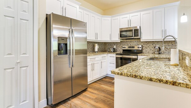 A modern kitchen with white cabinets, stainless steel appliances, a granite countertop, and a built-in microwave. - 11 Mi to Fort Myers River District: Suburban Haven (Lehigh Acres)