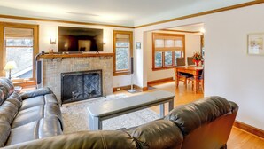 A living room with a fireplace, leather sofa, and a dining area with a table and chairs. - Charming Tudor-style Apt Near Green Lake! (Seattle)