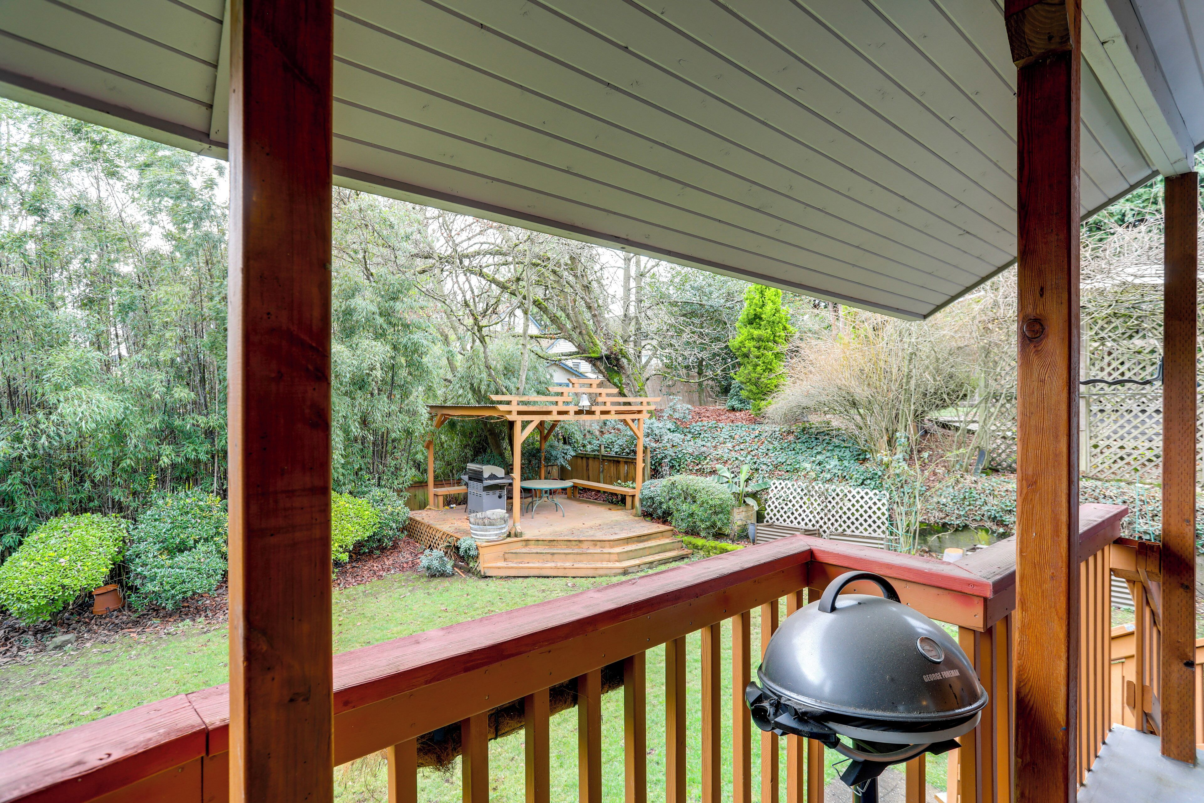 A wooden deck with a barbecue grill, a wooden pergola, and a garden with various plants and a wooden fence.