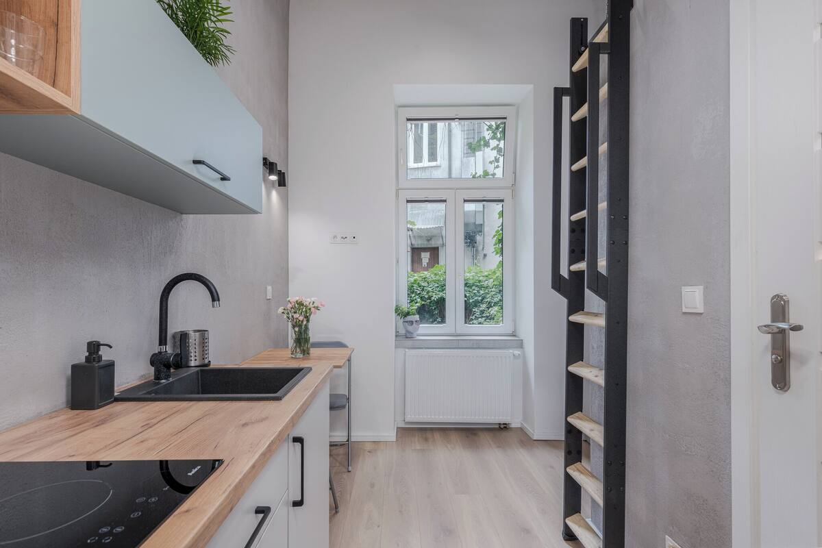 Une cuisine moderne avec un plan de travail en bois, un évier noir et une cuisinière intégrée. Une fenêtre offre une vue sur la verdure à l’extérieur.
