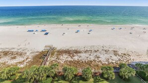 A beach with clear blue water, a sandy shore, and several blue umbrellas. - Regency Isle 1102 - Gulf Front Penthouse (Orange Beach)