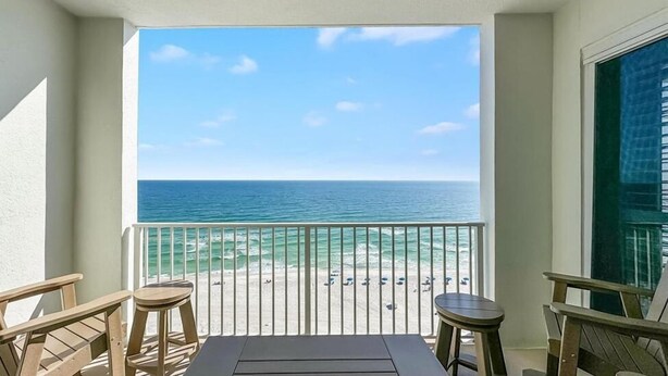 A balcony with a view of the ocean, two wooden chairs, and a table. - Regency Isle 1102 - Gulf Front Penthouse (Orange Beach)