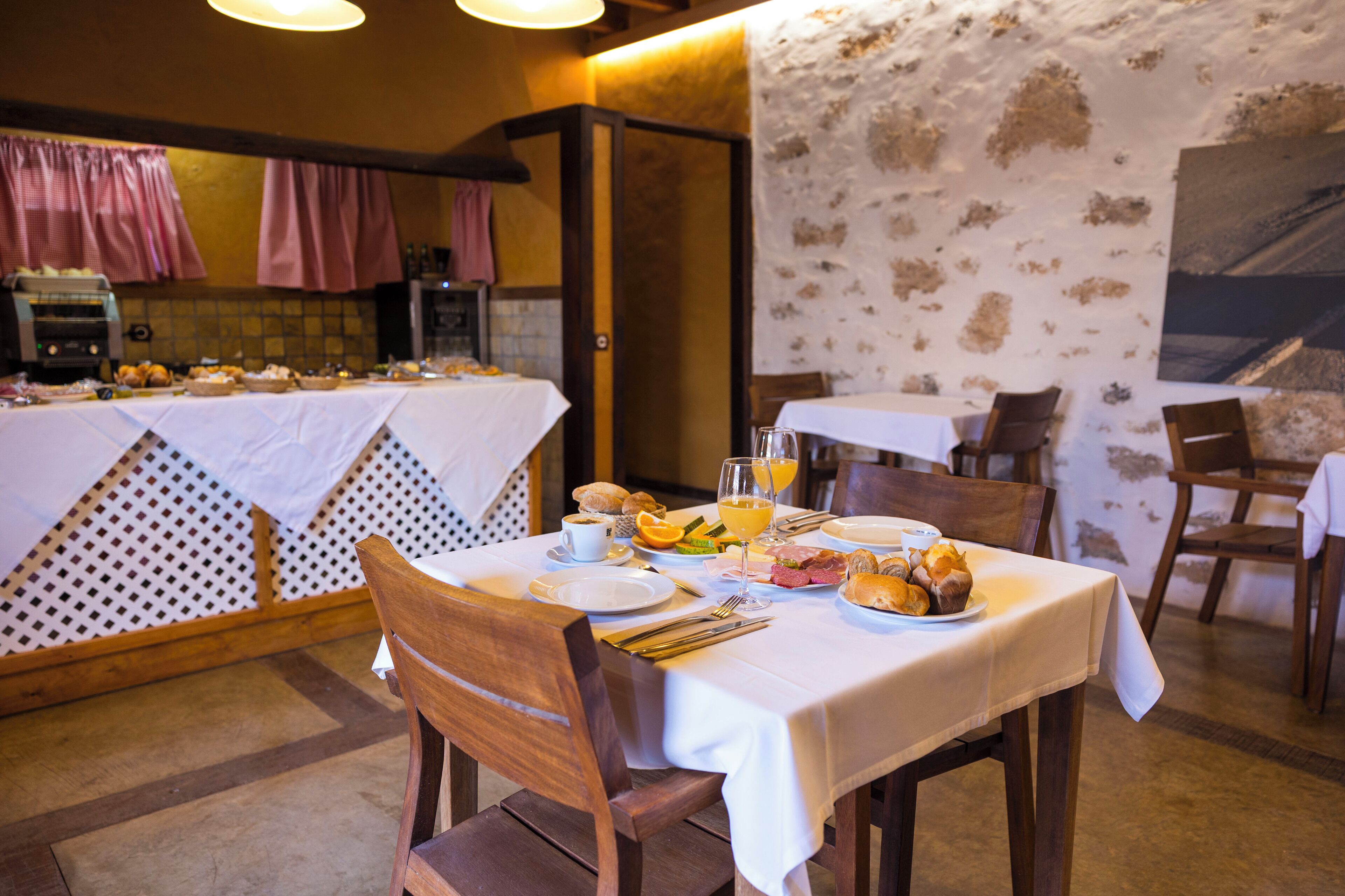 Un bufé de desayuno con diversas opciones de comida y bebidas, sillas de madera y un mantel blanco.