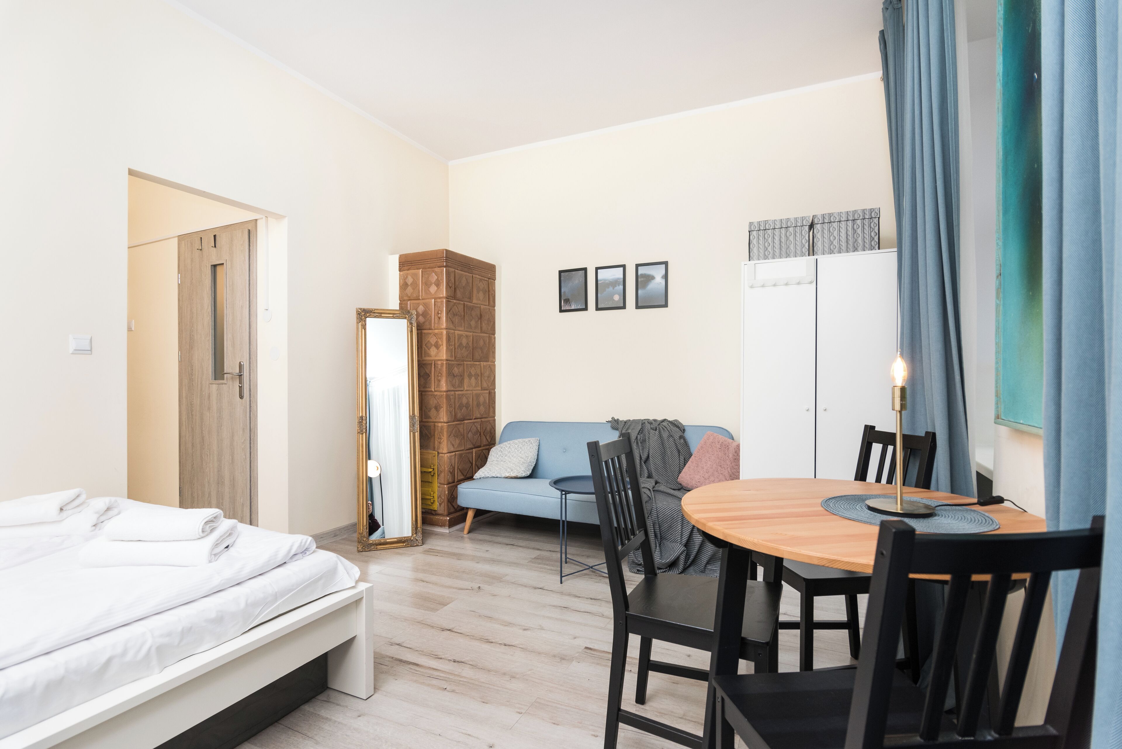 A bedroom with a bed, a wooden chest of drawers, a blue sofa, a dining table with chairs, and a mirror.