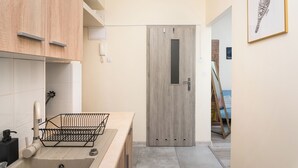 Une salle de bain moderne avec un meuble-lavabo en bois, un évier et un miroir. Un tableau encadré orne le mur, et une porte avec une petite fenêtre est également présente.