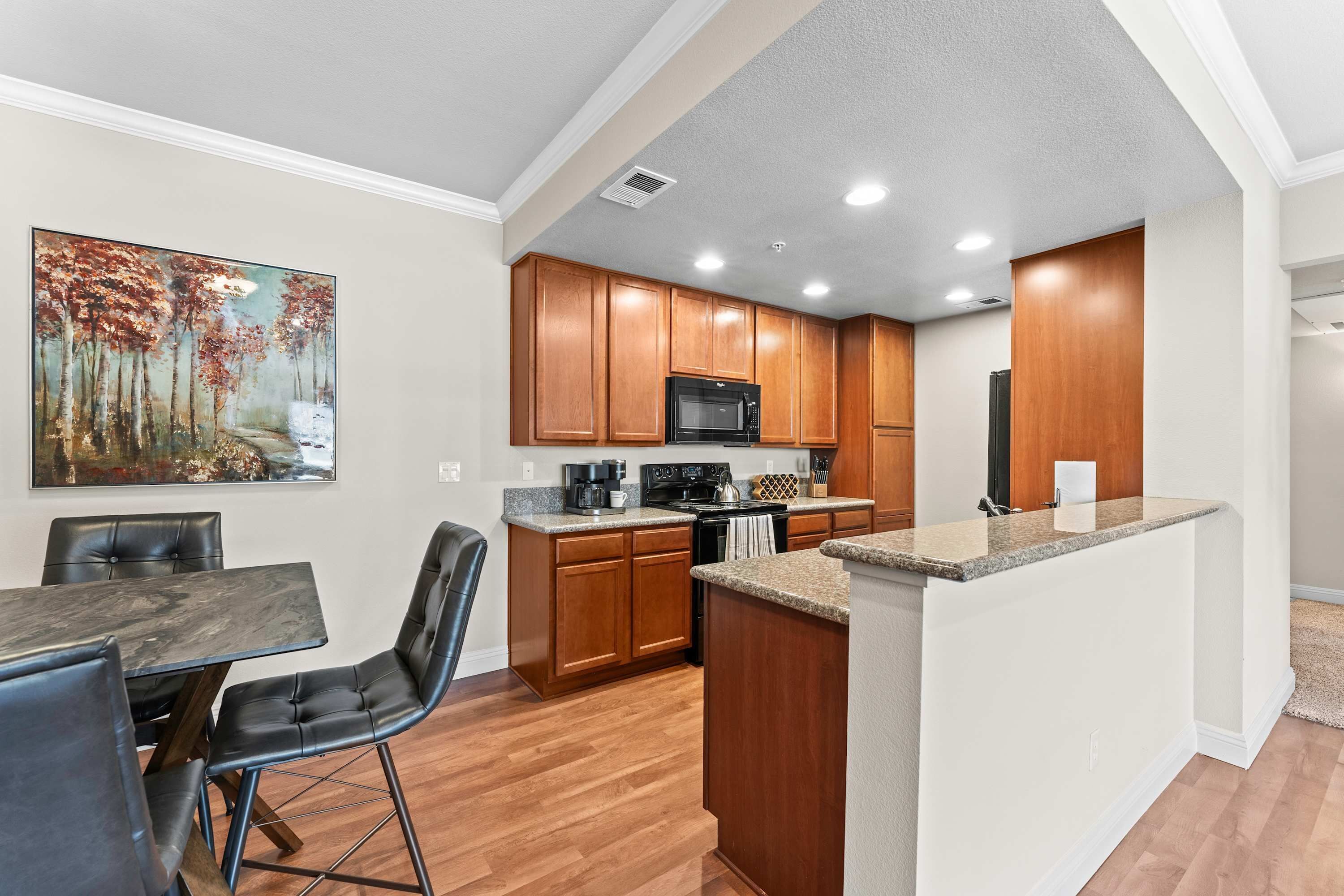 A modern kitchen with wooden cabinets, a granite countertop, and a dining area with a table and chairs.