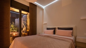 Een moderne slaapkamer met een groot bed, een nachtkastje en een glazen deur naar een buitenruimte met een lamp en kaarsen.