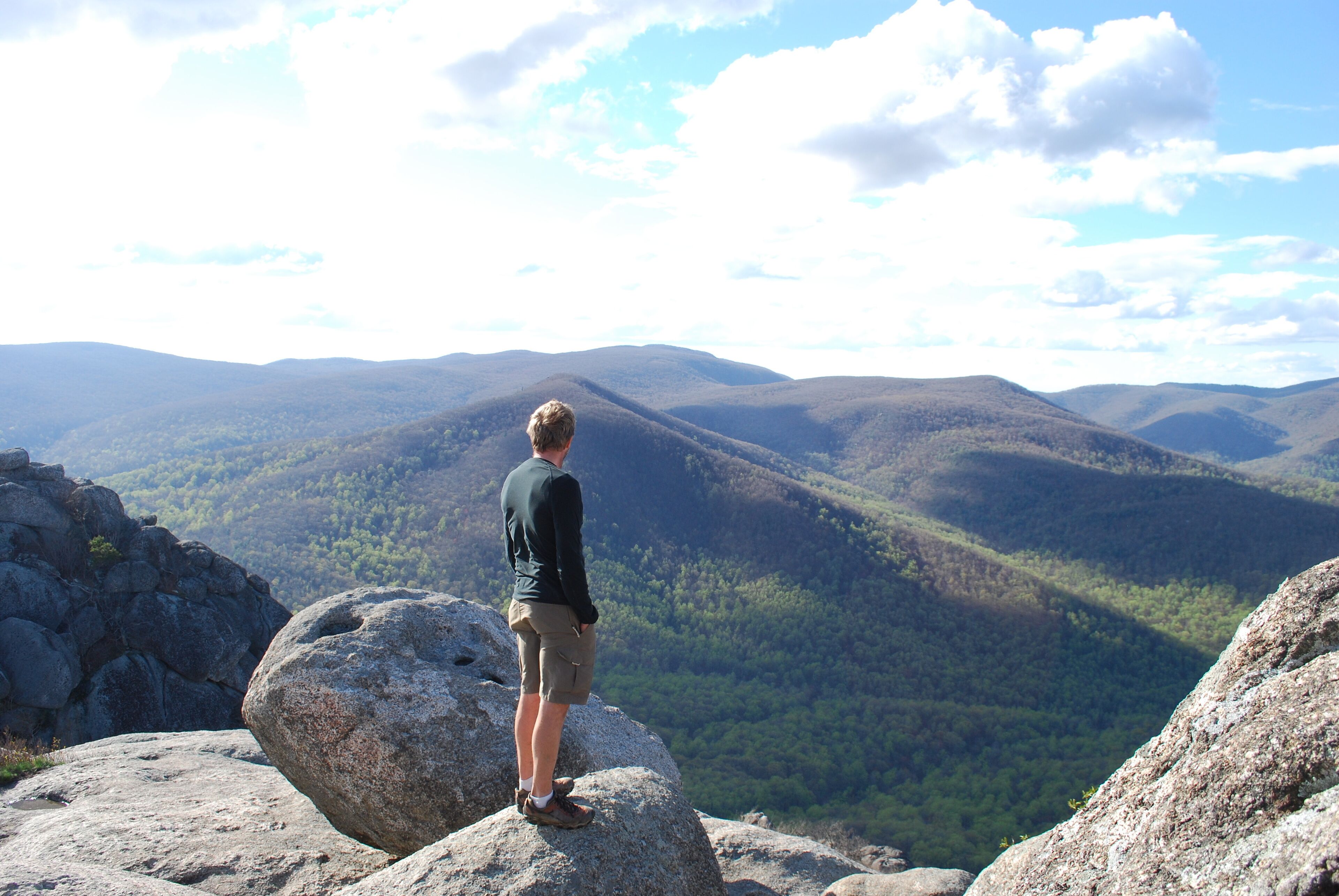 A person standing on a rock overlooking a mountainous landscape.