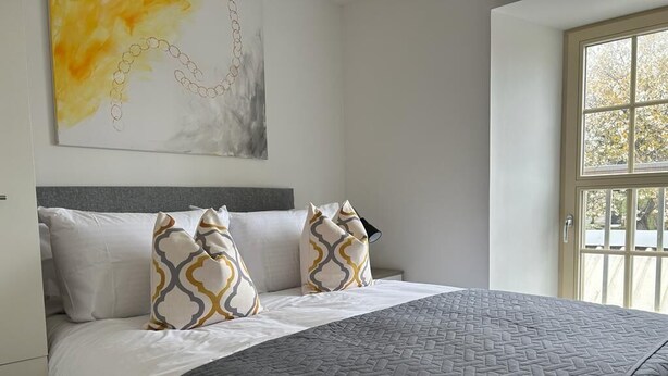 Une chambre à coucher avec un lit, des oreillers, une couvre-lit matelassé, un tableau au mur et une fenêtre donnant sur un paysage.