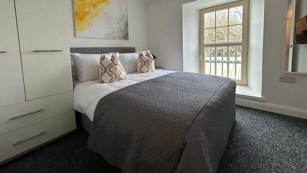 A bedroom with a bed, a window, a wardrobe, and a painting on the wall.
