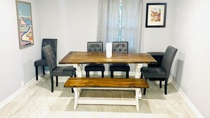 Een eetgedeelte met een houten tafel, zwarte stoelen, een bank en een witte vloer.
