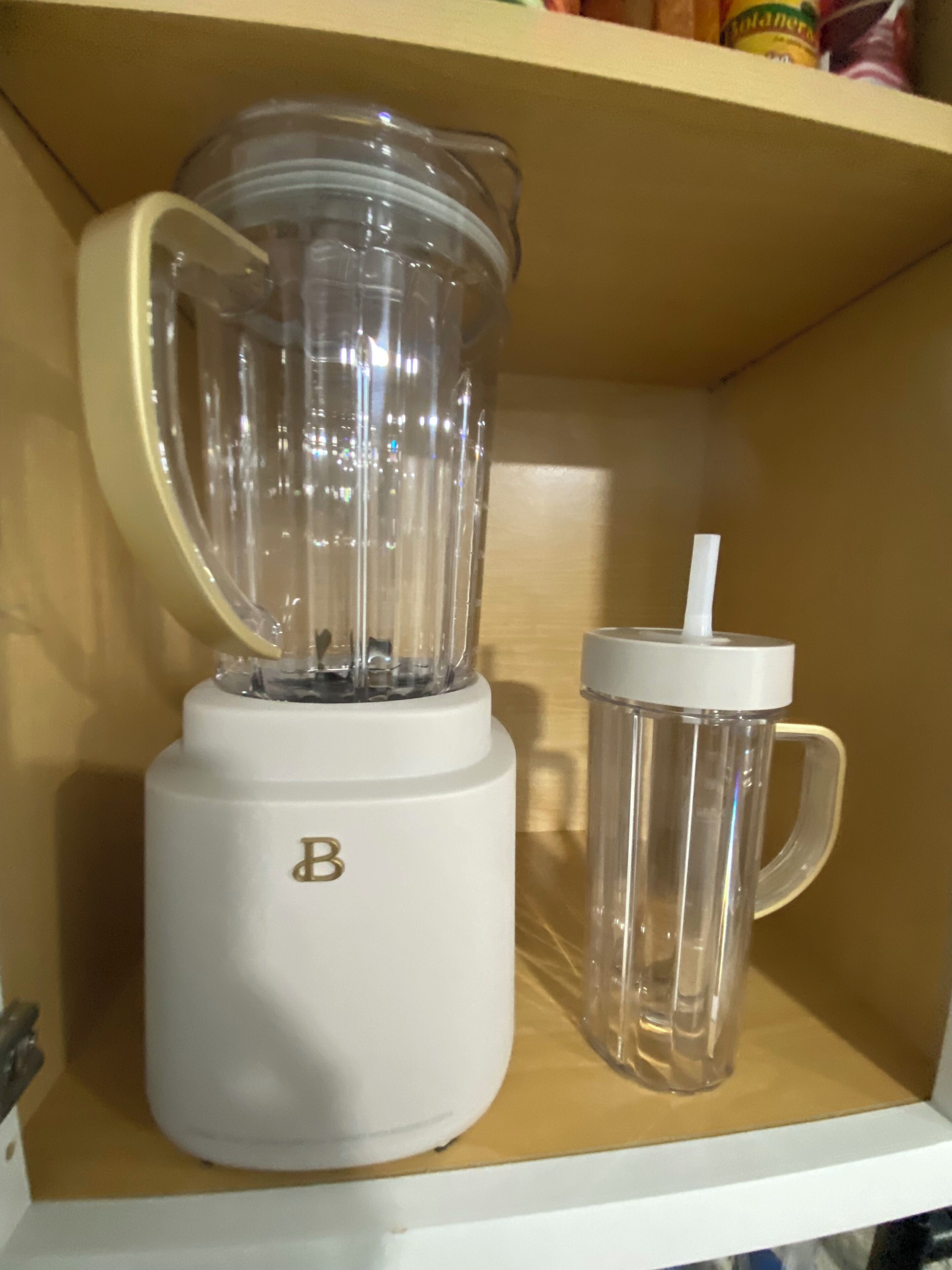 Ein weißer Mixer mit einer transparenten Kanne und einer passenden Tasse auf einem Regal.