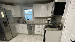 Een moderne keuken met witte kastjes, een roestvrijstalen koelkast en een raam dat voor natuurlijk licht zorgt.