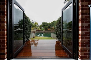 Une vue à travers une porte vitrée donnant sur une terrasse en bois, avec une pelouse et une clôture.