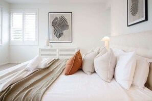 A neatly arranged bedroom with a bed, pillows, a bedside table, and a framed artwork on the wall.