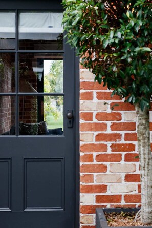 A dark grey door with a window, a brick wall, and a tree.