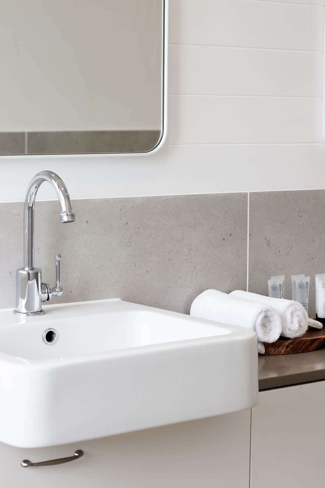 A modern bathroom with a white sink, chrome faucet, and a mirror above it.