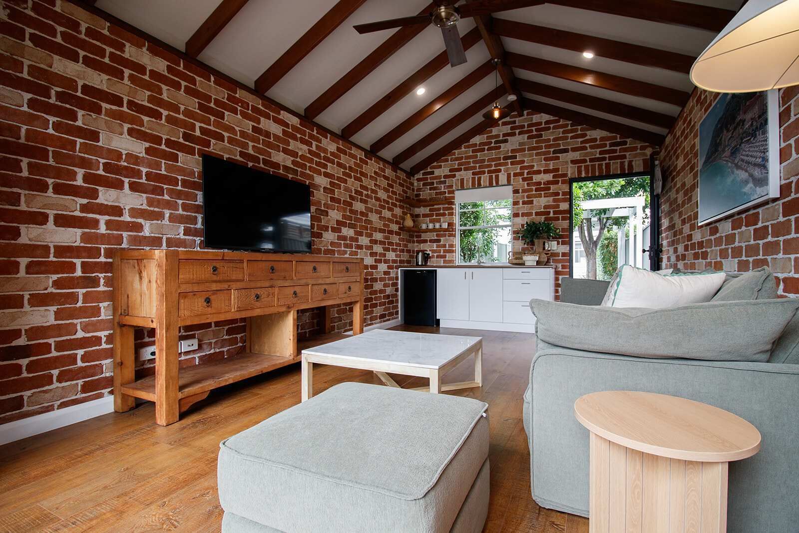 Un salon chaleureux avec un mur en briques, des meubles en bois, un téléviseur à écran plat et une fenêtre donnant sur un espace verdoyant.