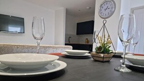 A dining table with plates and glasses, a small plant, and a clock on the wall. - Seaside Escape Apartment in Southend-on-sea (Southend-on-Sea)