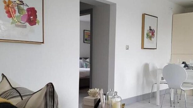 A modern living room with a sofa, a coffee table with decorative items, and a dining area with chairs and a table. - Seaside Escape Apartment in Southend-on-sea (Southend-on-Sea)