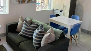 A modern living room with a green sofa, blue chairs, a white table, and a large abstract painting. - Seaside Escape Apartment in Southend-on-sea (Southend-on-Sea)