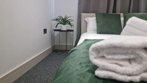 A hotel room with a bed, a small table with a plant, and a green blanket. - Seaside Escape Apartment in Southend-on-sea (Southend-on-Sea)