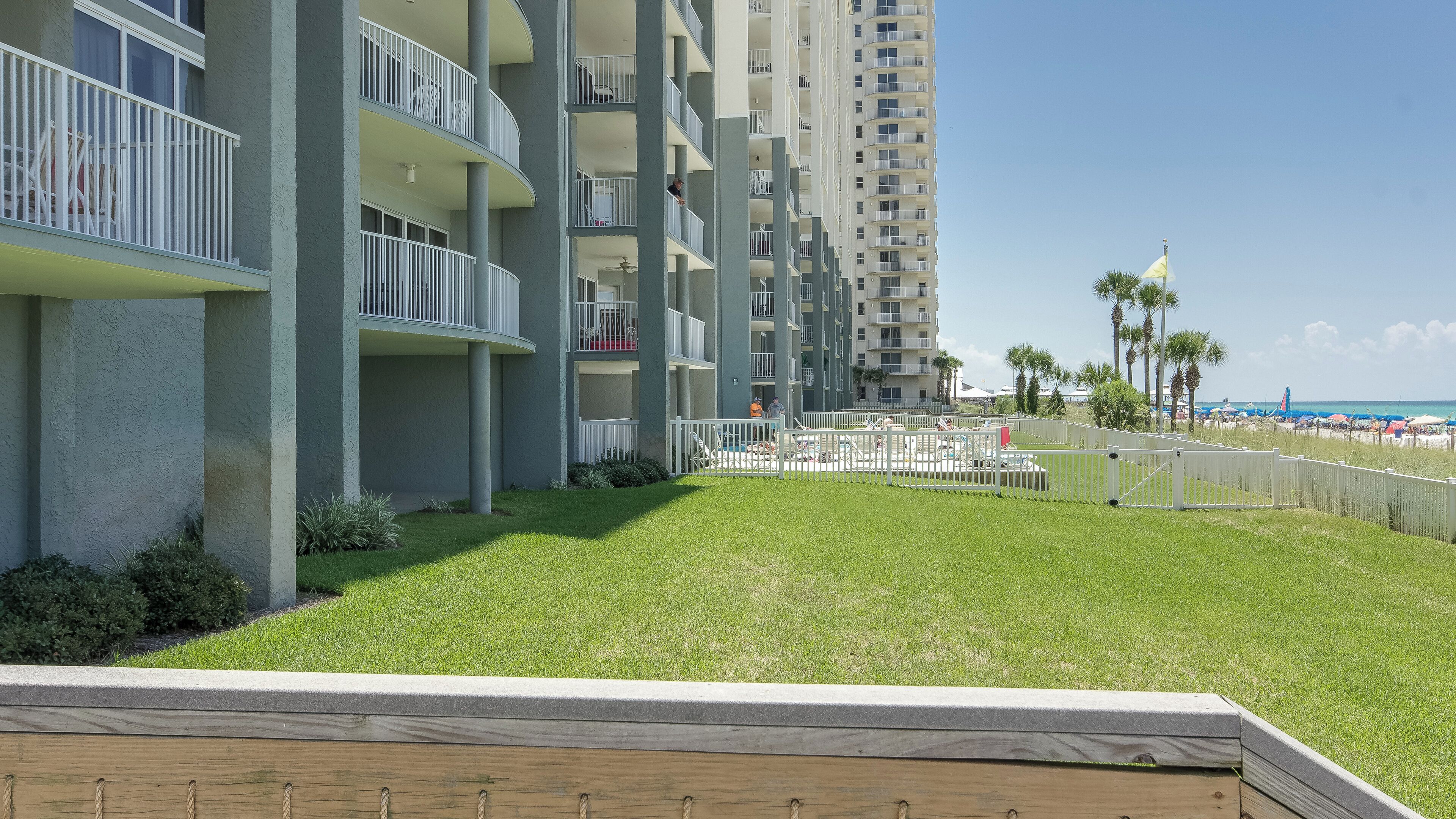 A multi-story hotel with balconies, a pool area, and a view of the beach.