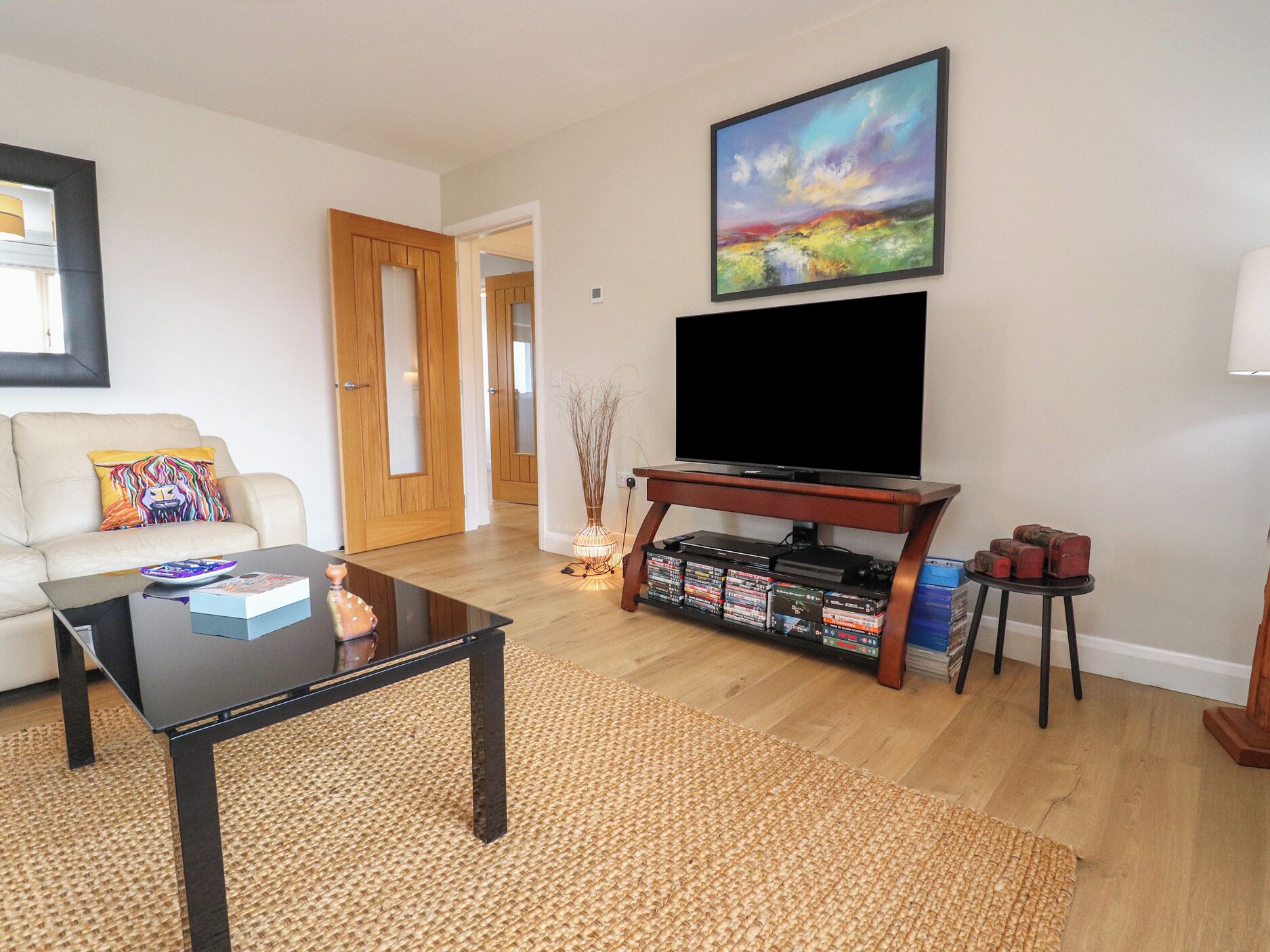 Un salon avec un téléviseur à écran plat posé sur un meuble, une table basse, un canapé agrémenté d’un coussin coloré et une bibliothèque contenant des DVD.