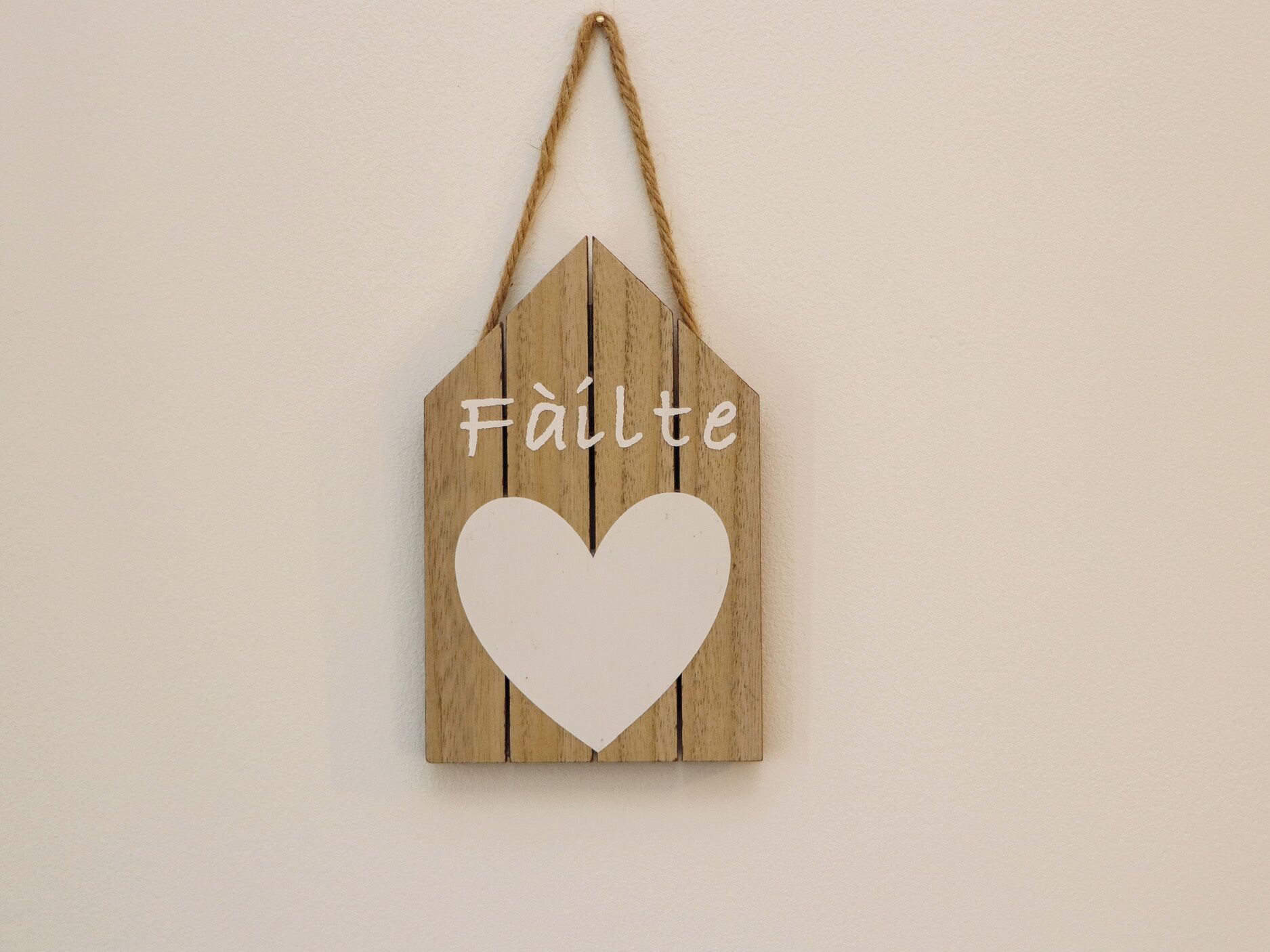 Un cartello di legno con un cuore e la scritta 'Fäilte' appeso al muro.